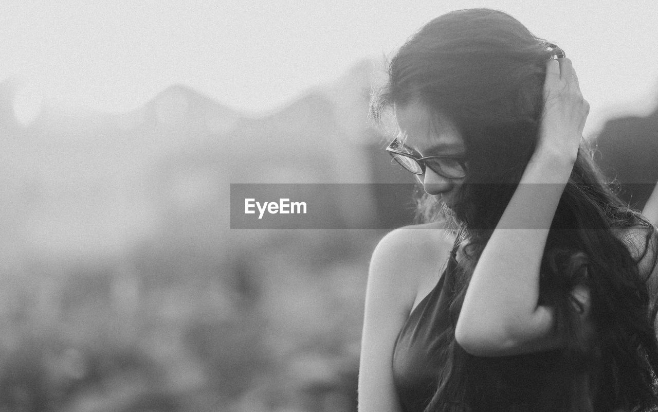 one person, adult, women, black and white, black, white, young adult, monochrome photography, portrait, hairstyle, monochrome, nature, lifestyles, emotion, long hair, glasses, female, waist up, headshot, person, outdoors, land, focus on foreground, leisure activity, environment, contemplation, portrait photography, day, sadness, looking, sky, clothing, summer, mountain, standing