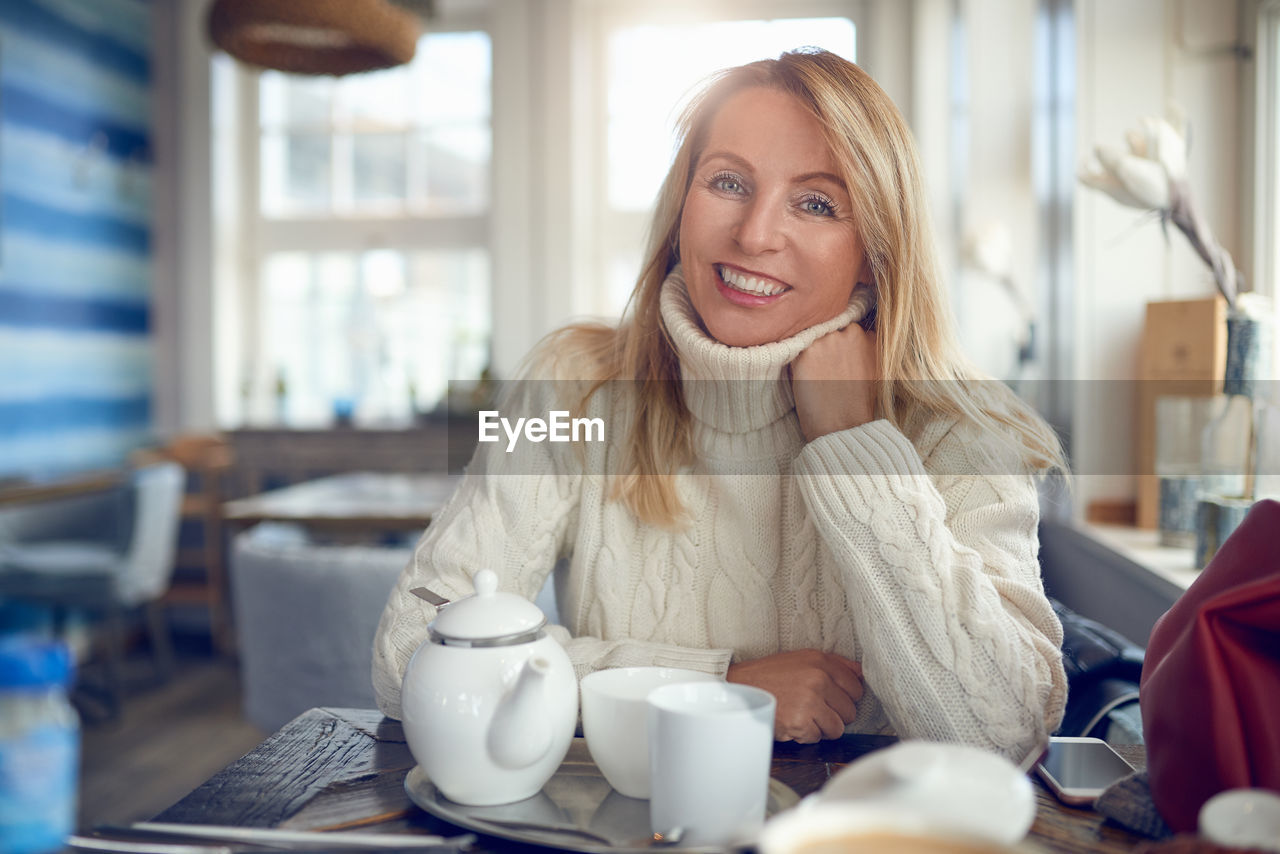 Portrait of smiling woman sitting with coffee on table at home