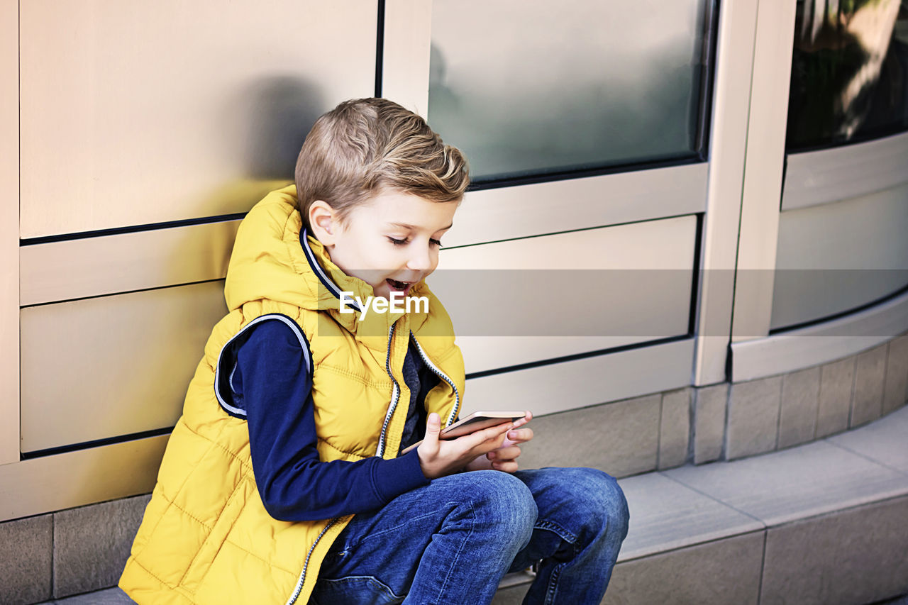 Happy kid using mobile phone while relaxing outdoors.