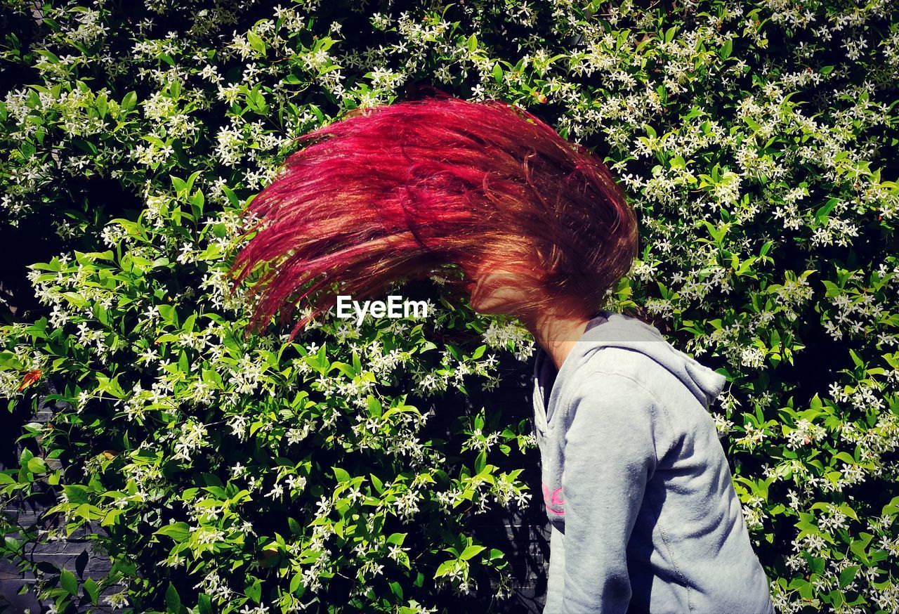 Side view of teenage girl tossing hair while standing against plants