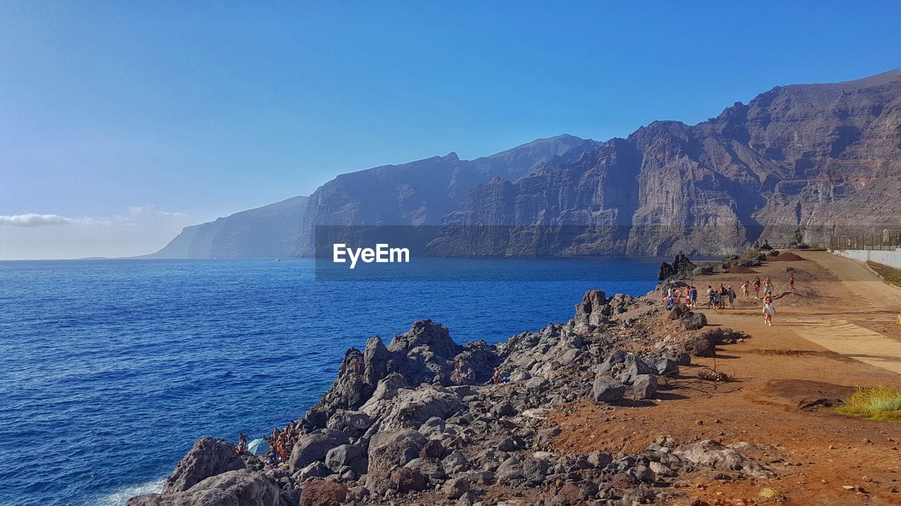 Scenic view of rocky cliff against clear blue sky