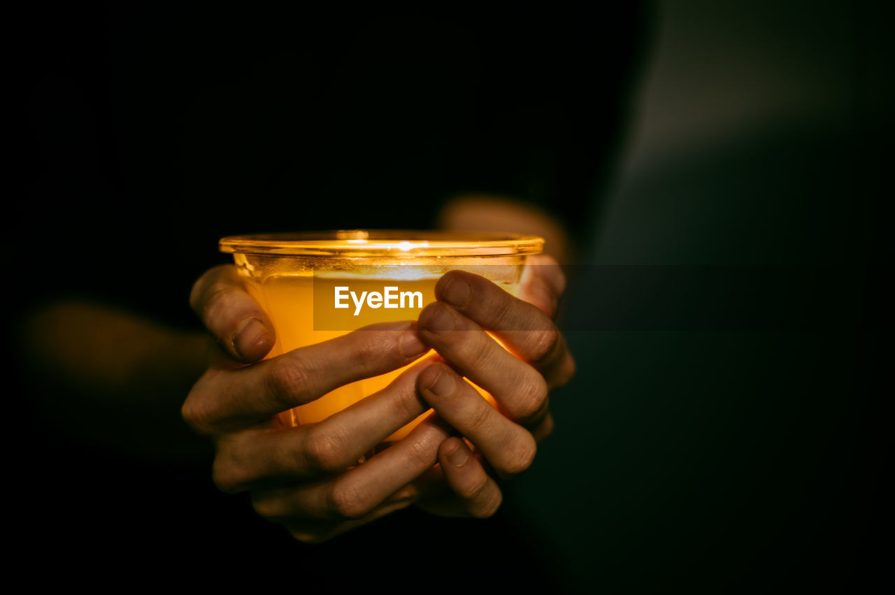 Midsection of person holding tea light candle in darkroom