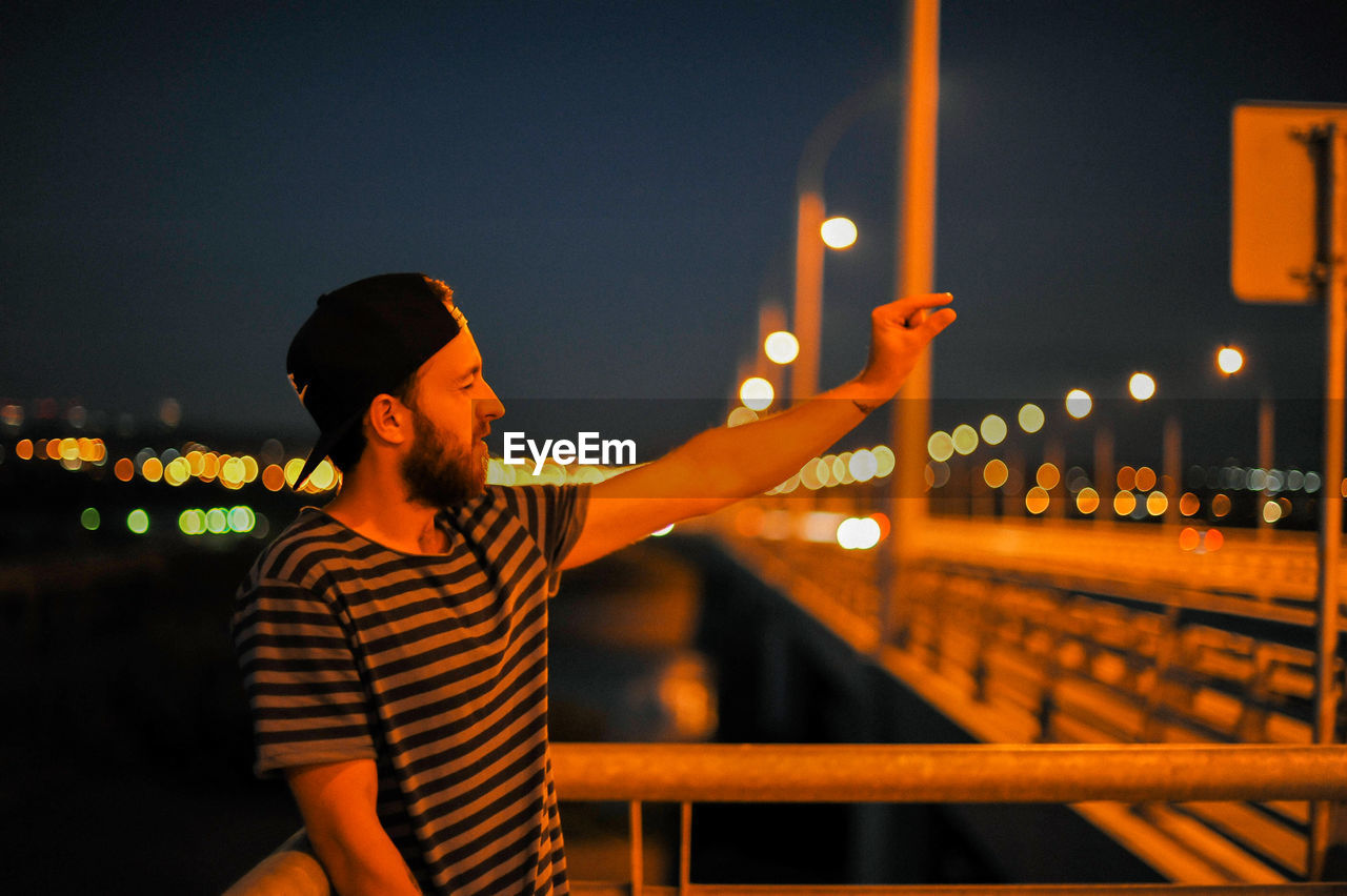 Young man gesturing on bridge at night