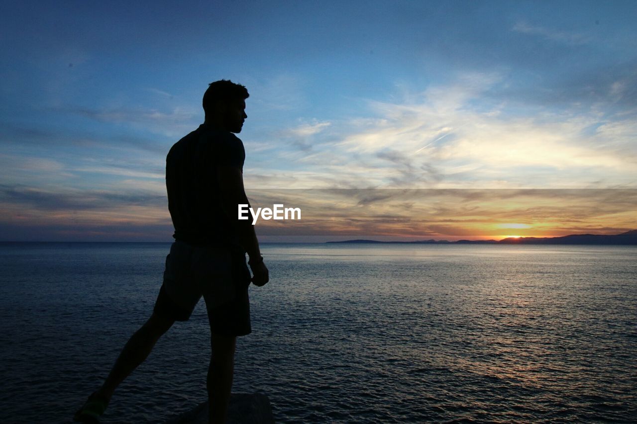 Silhouette man looking at sea during sunset