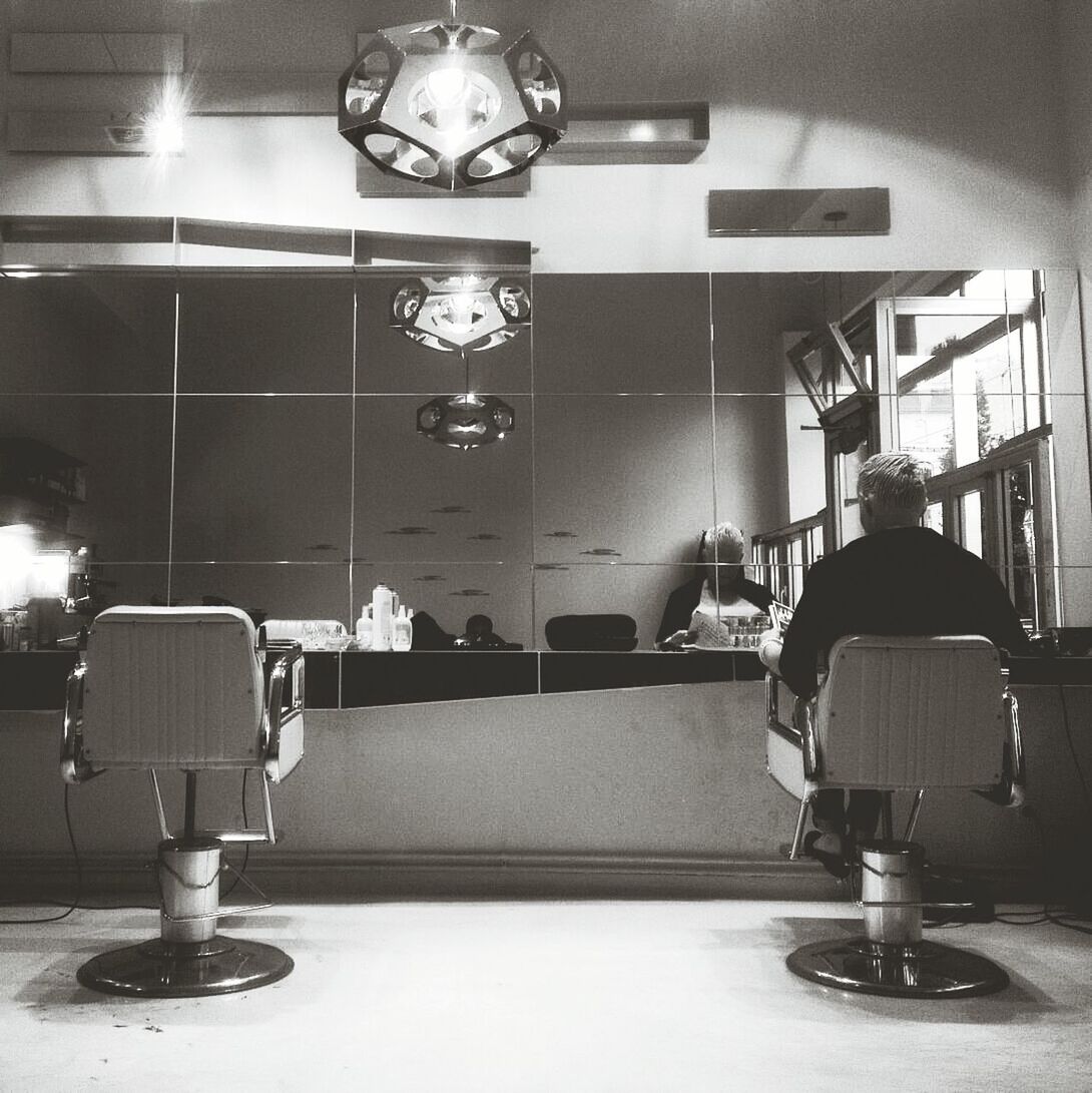 Rear view of woman sitting on chair with reflection in mirror at hair salon
