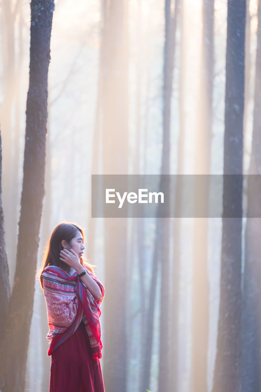 Young woman standing against trees