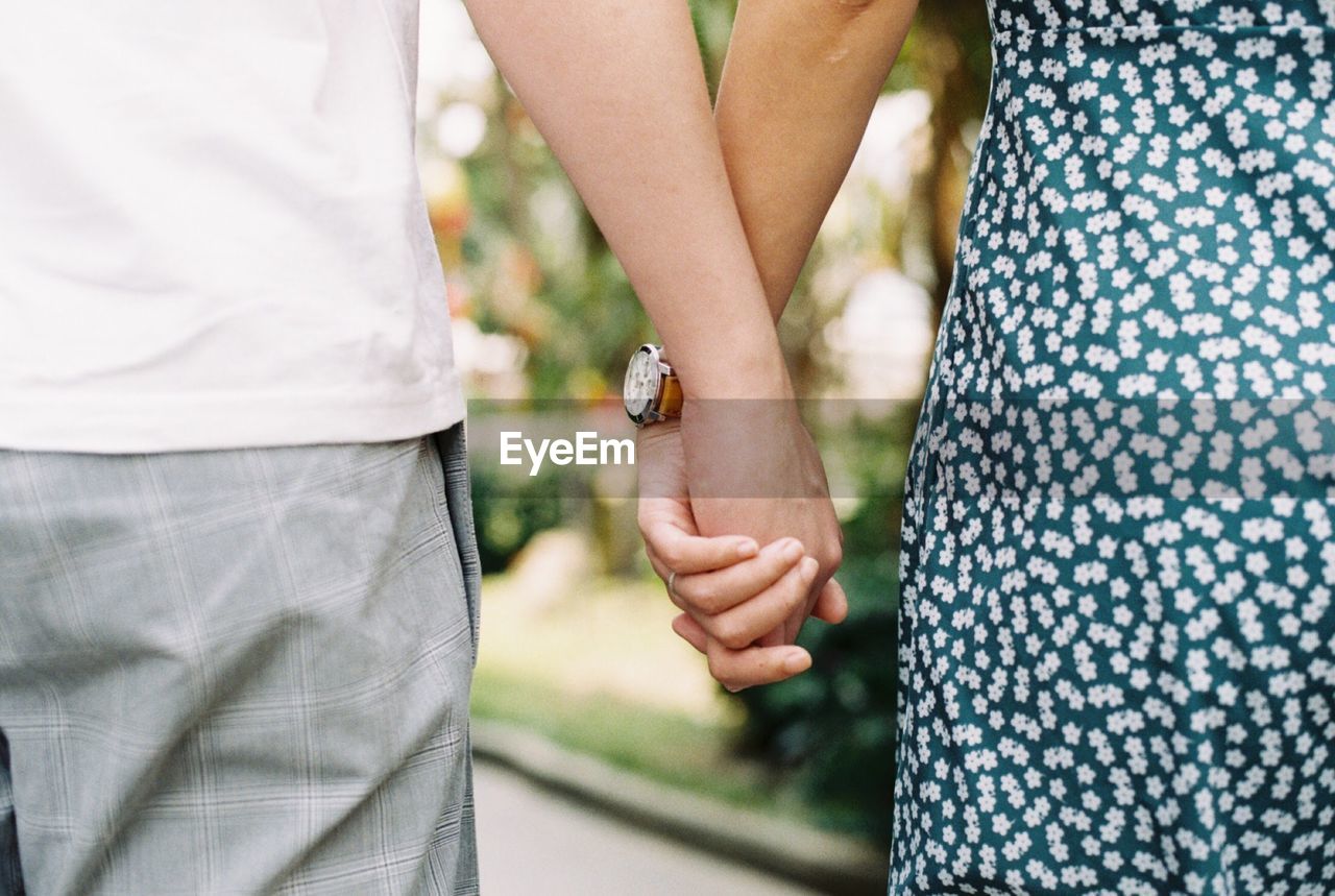 Midsection of couple holding hands while standing outdoors