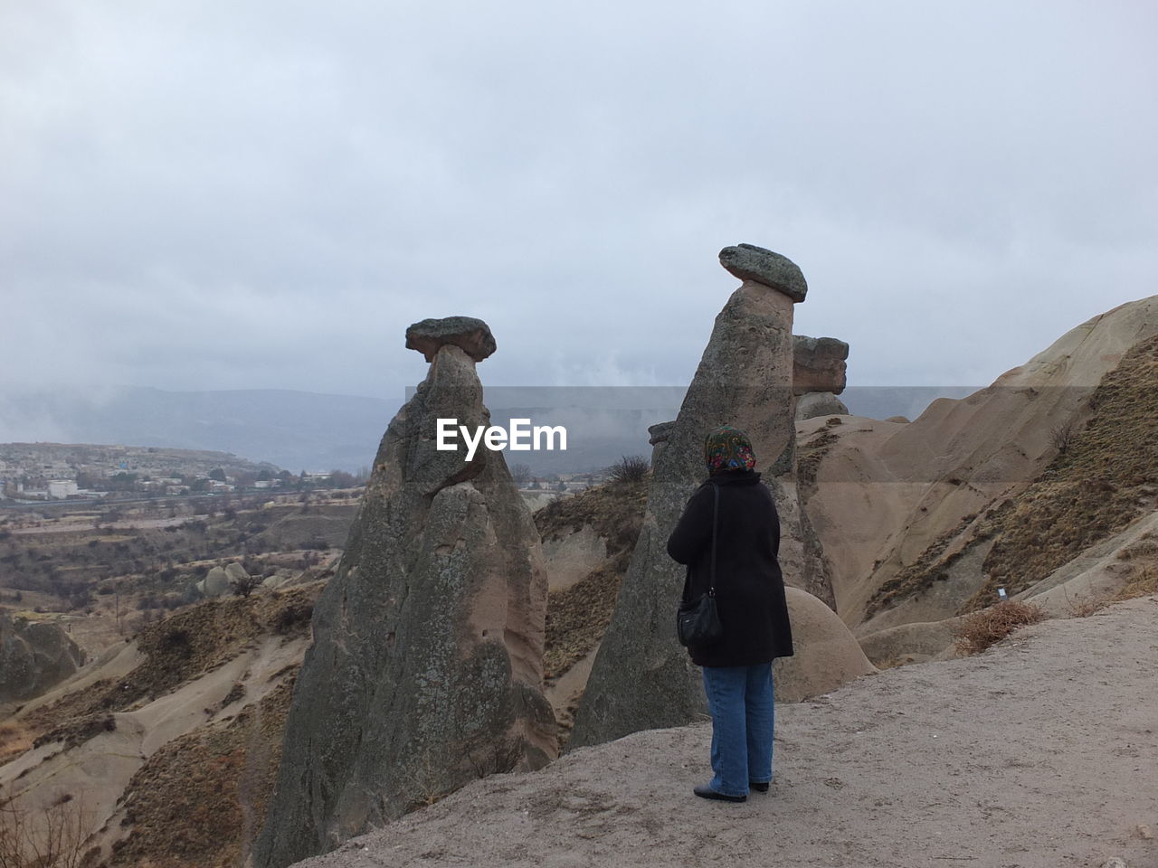 REAR VIEW OF MAN STANDING ON ROCK AGAINST CLOUDY SKY