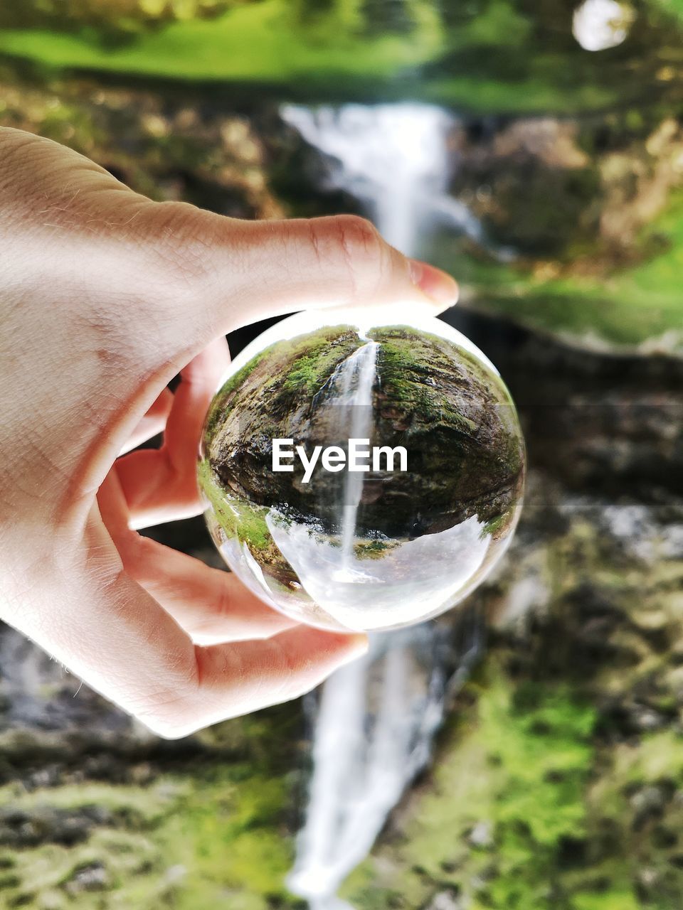 Cropped hand holding crystal ball with reflection of waterfall 