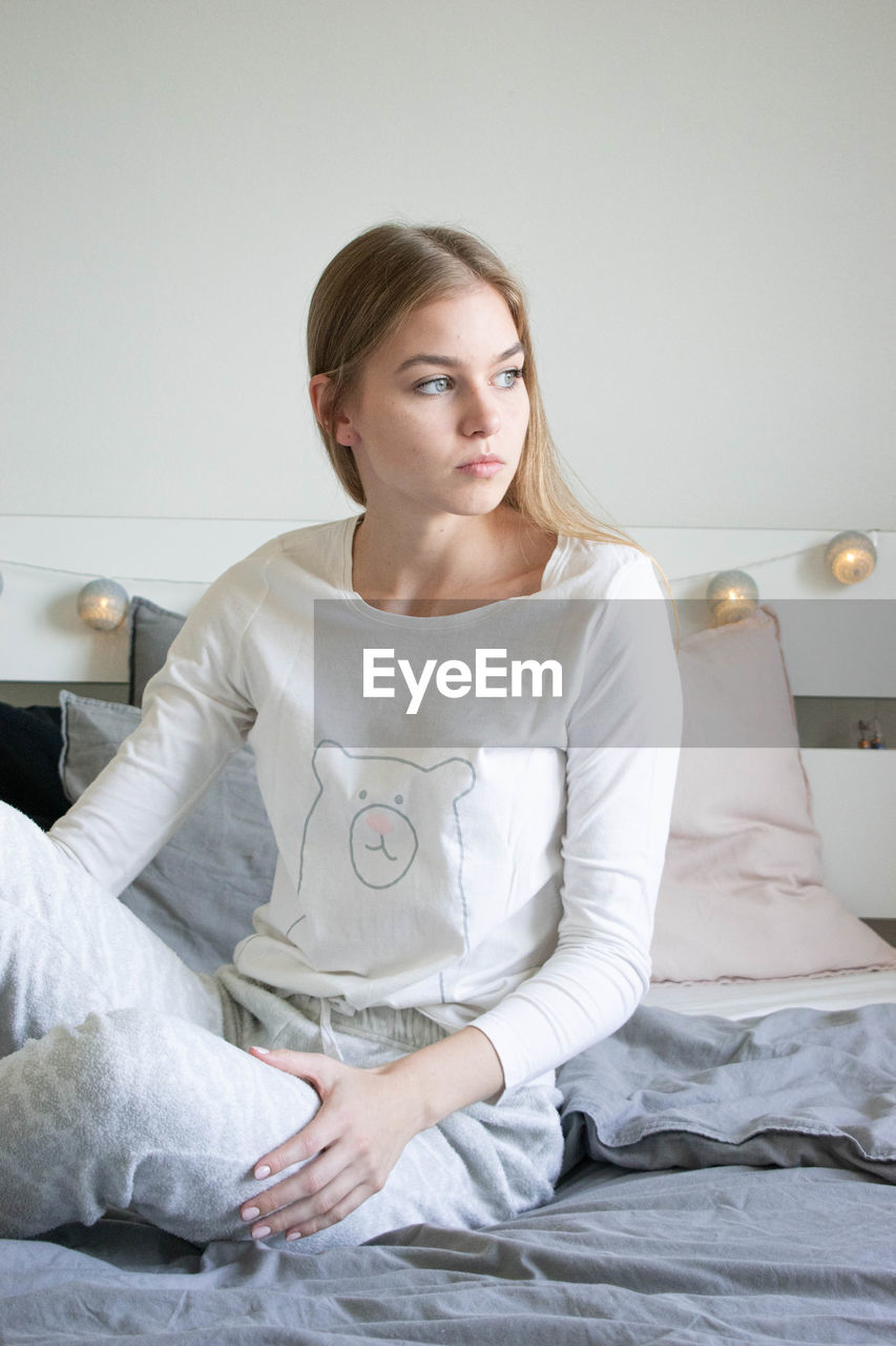 PORTRAIT OF YOUNG WOMAN SITTING ON BED