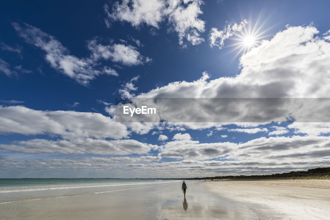 Australia, south australia, robe, summer clouds over silhouette of female tourist walking alone along fox beach