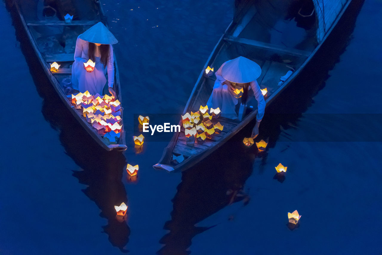 High angle view of women floating lighting equipment on lake at night