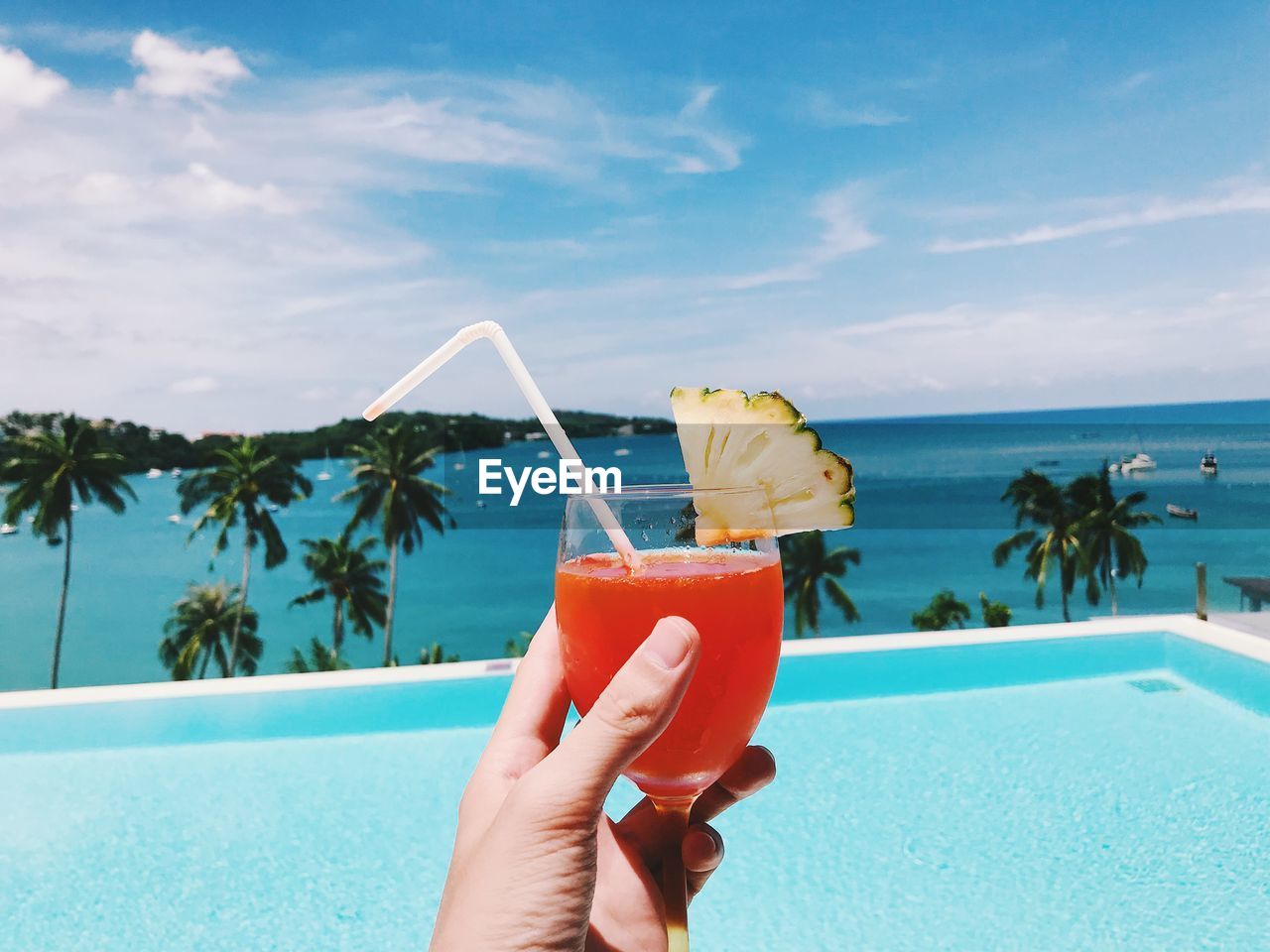 Cropped hand holding drink by infinity pool with sea in background