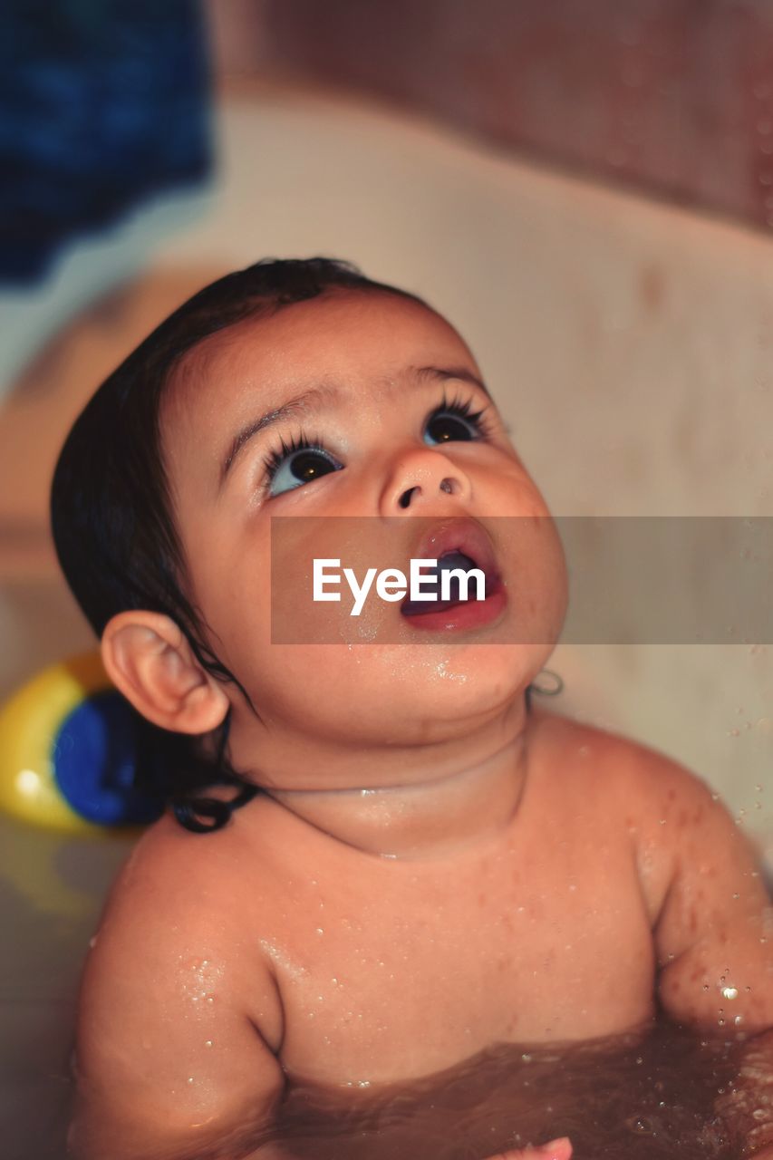 Close-up of cute baby girl looking up while bathing in bathtub