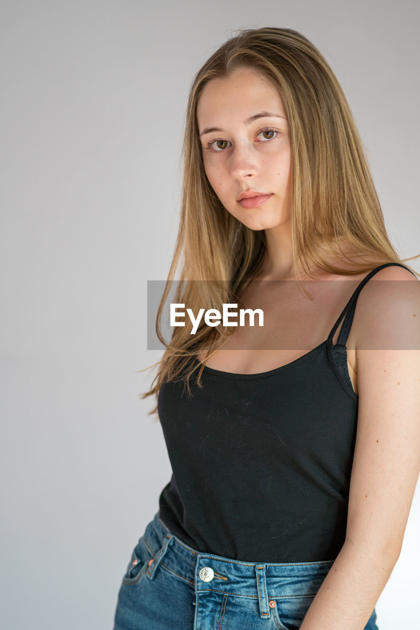 Portrait of an attractive teenage girl wearing camisole posing looking at camera on grey background