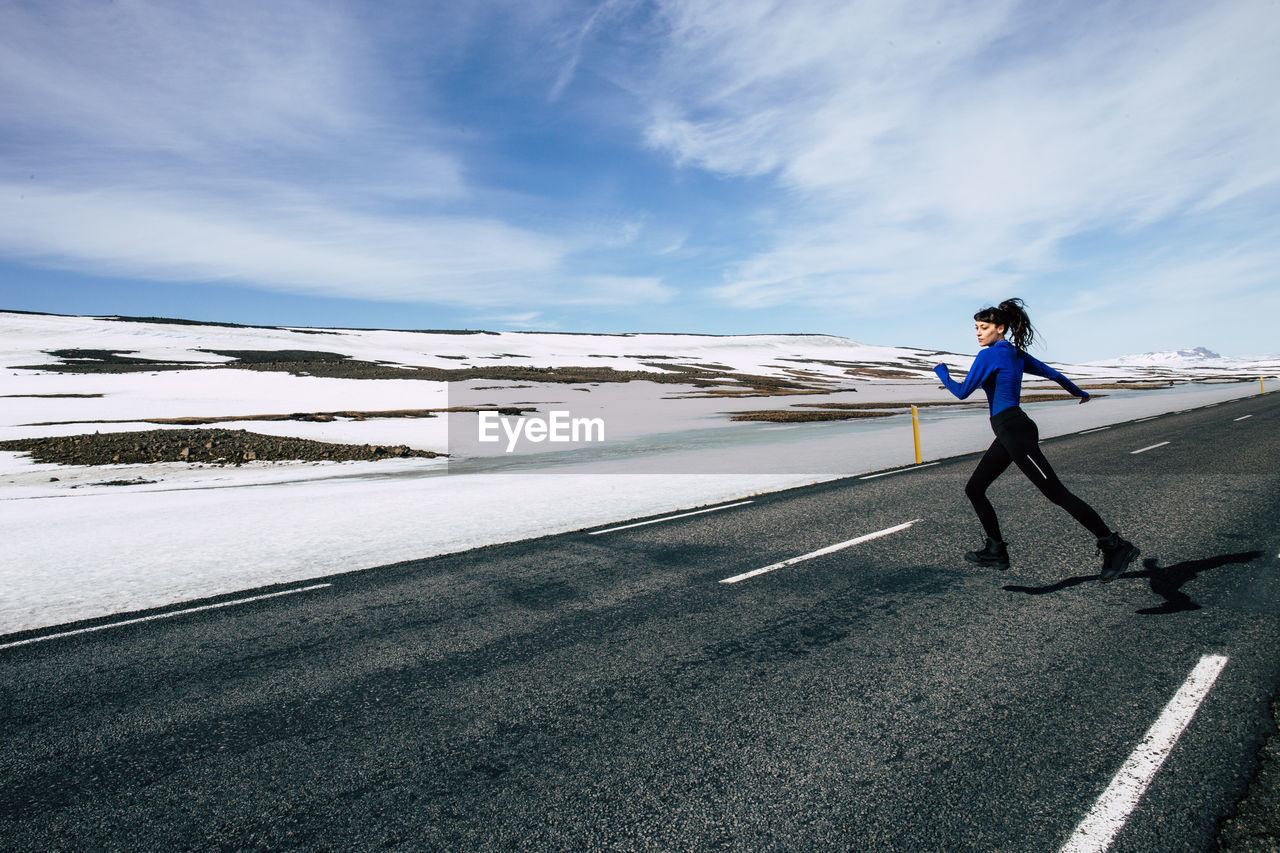 Woman running on road against sky during winter