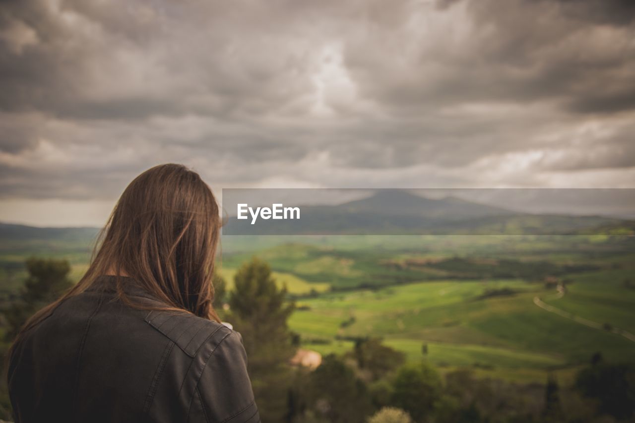 Woman looking at mountains against cloudy sky