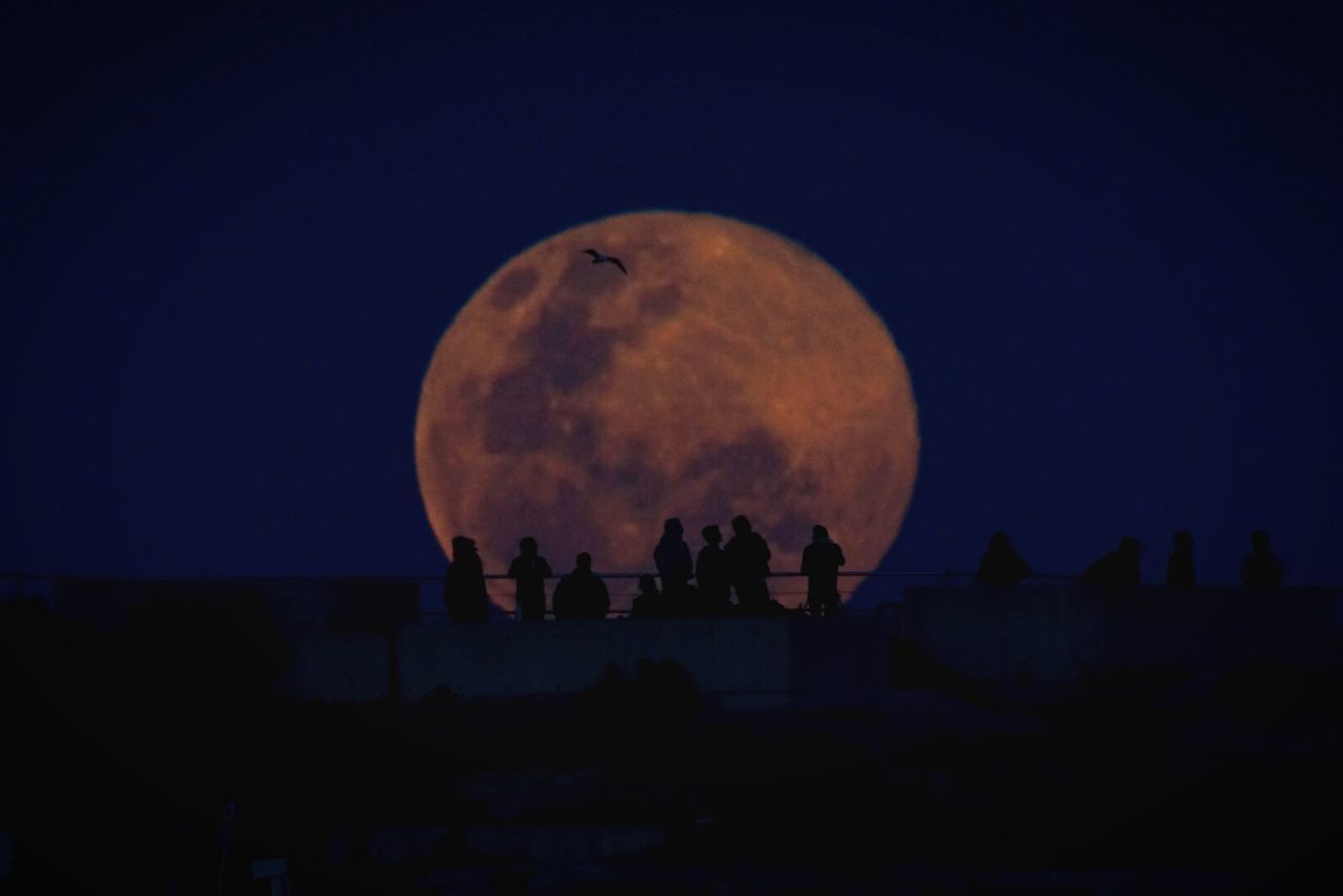 Silhouette people on bridge against full moon at night