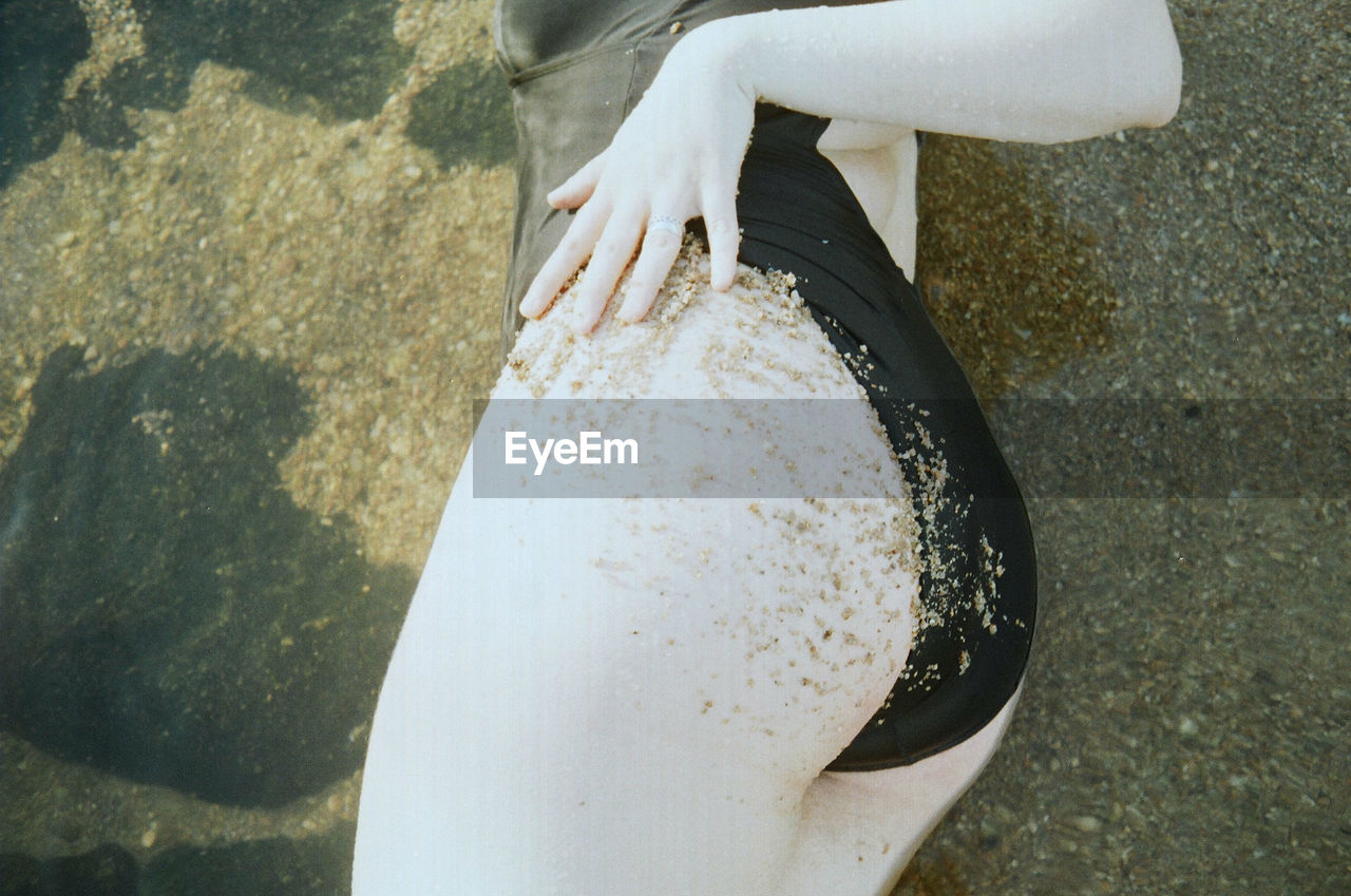 Midsection of sensuous woman in swimwear relaxing at sandy beach