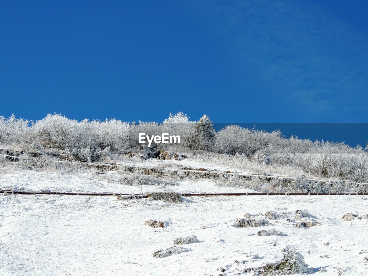 Snow covered landscape against clear blue sky