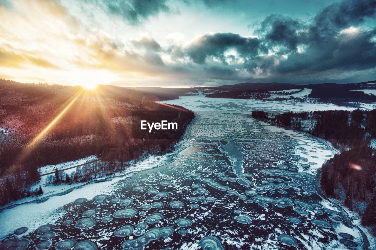 Snow covered landscape against sky during sunset