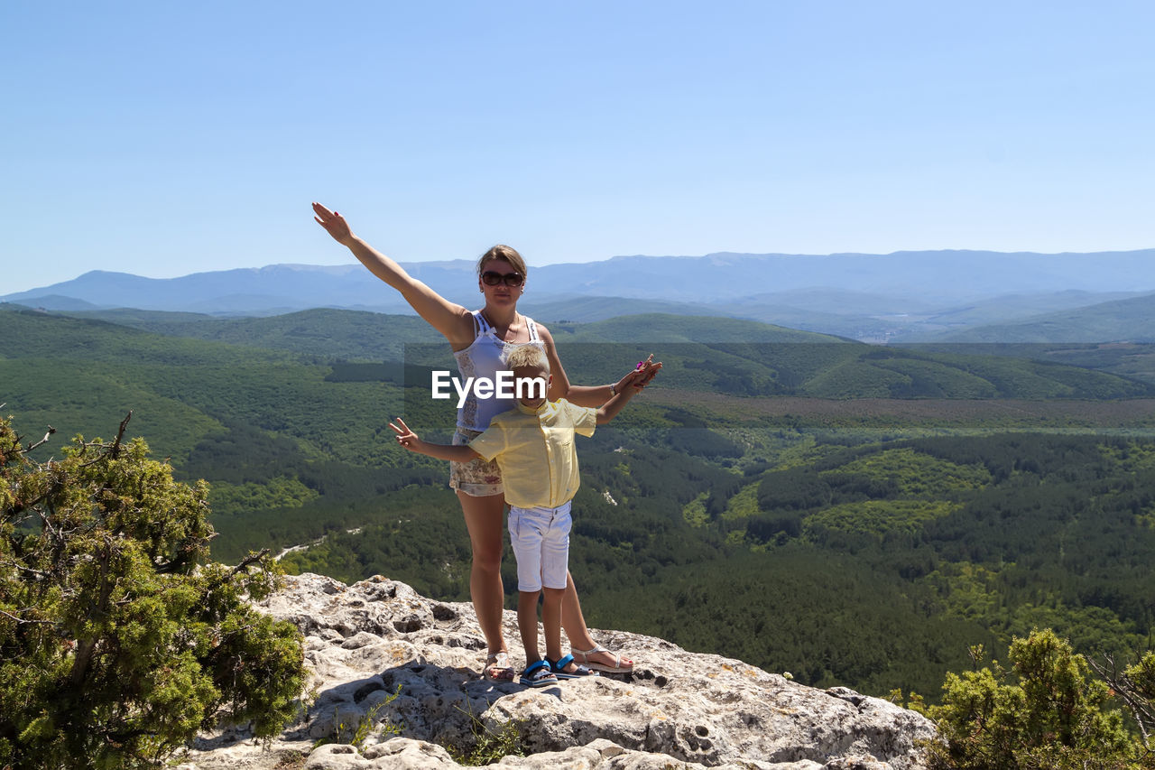 Fearless woman with adorable happy boy stand on steep edge of limestone plateau overlooking valley