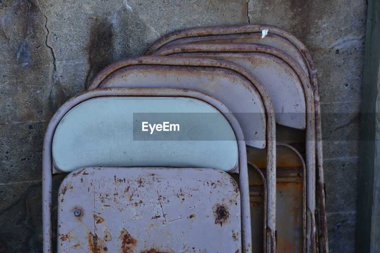 Close-up of rusty folded metal chairs against wall