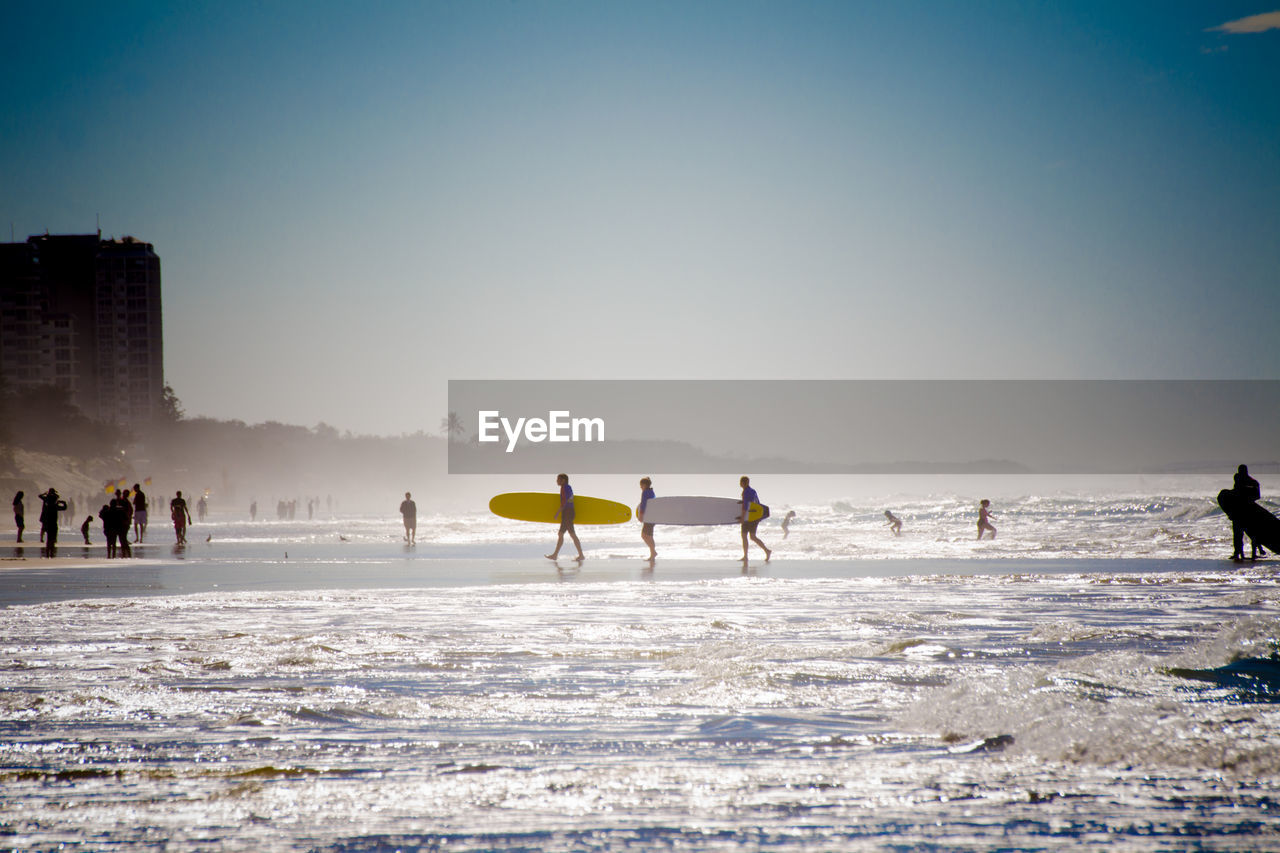 People enjoying at beach against clear sky