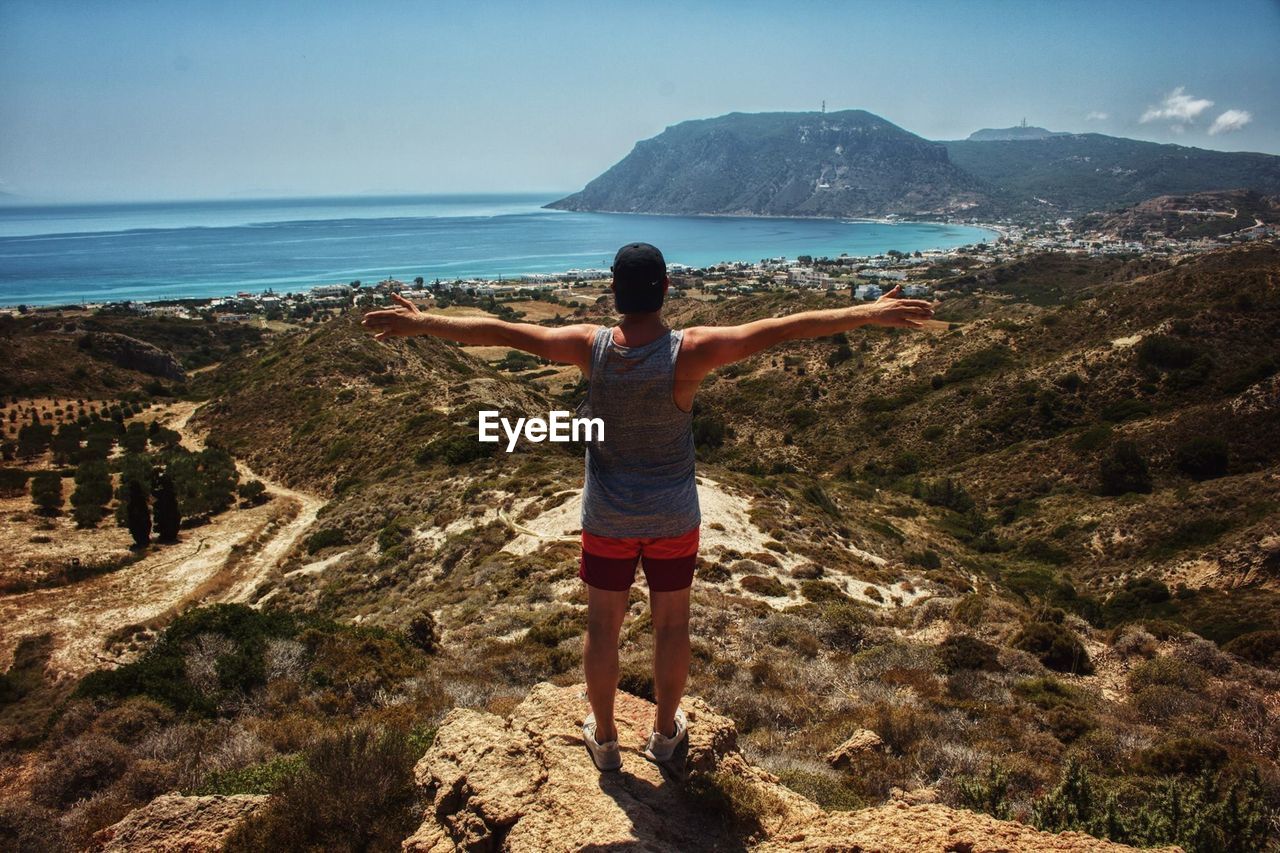 Rear view of man standing on cliff near sea