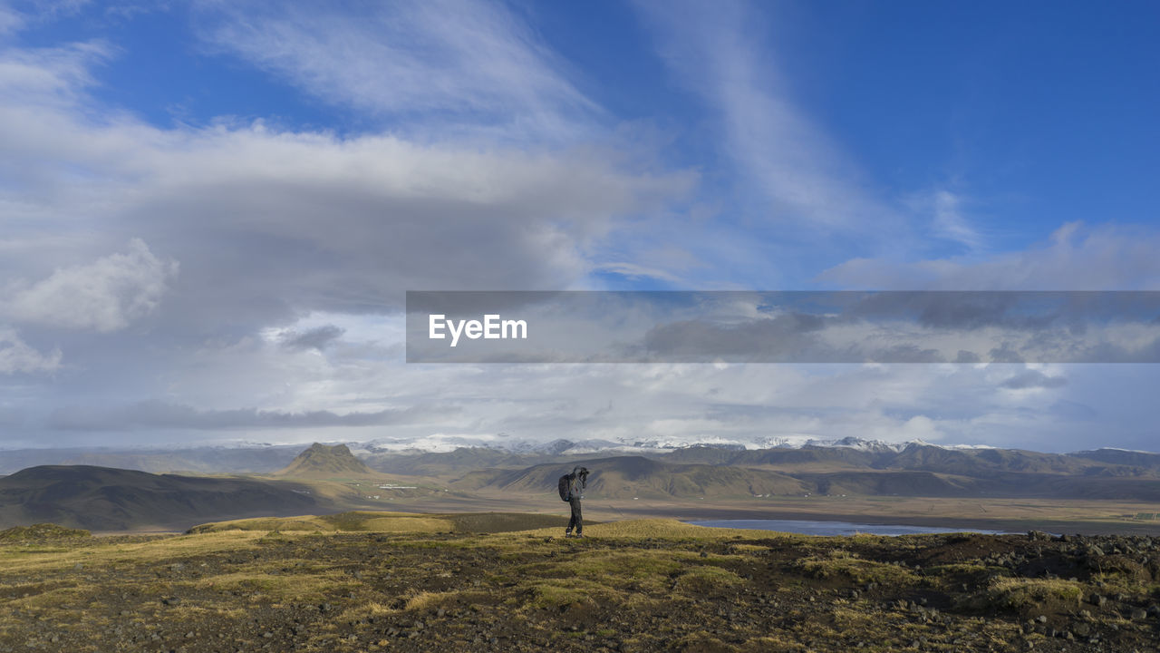 Distant image of person standing on field against cloudy sky