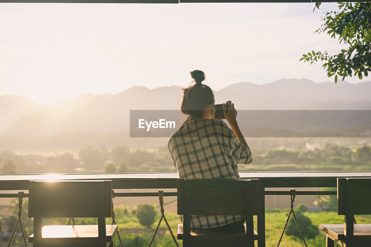 Rear view point of young woman using camera with beautiful sunset