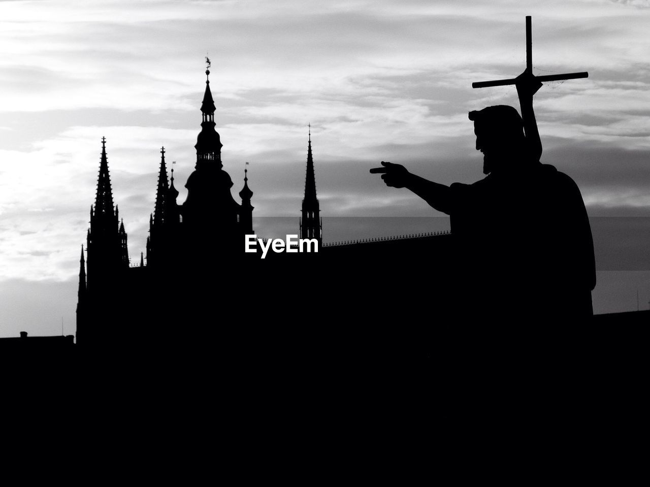 Silhouette statue pointing towards church against sky