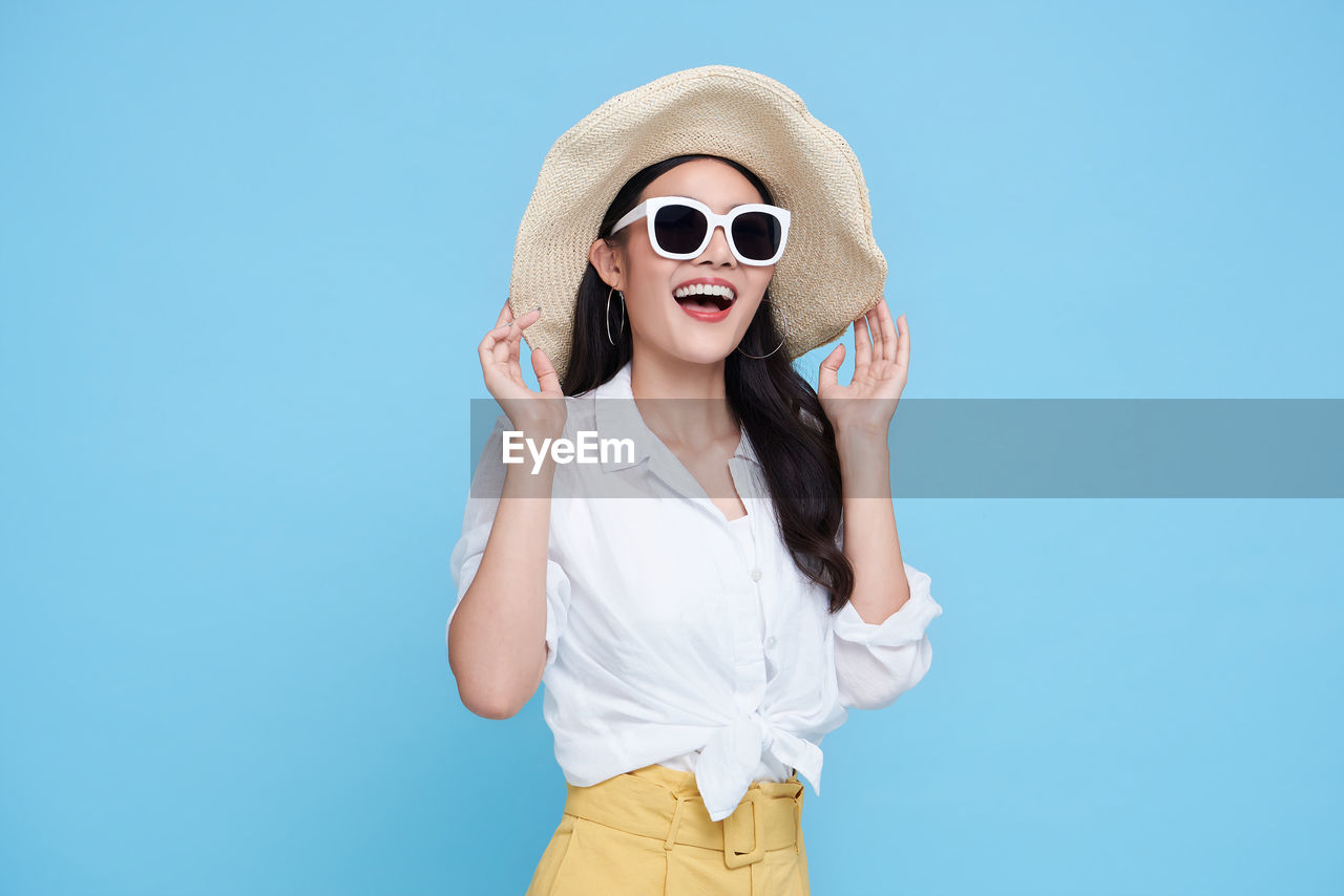 Young woman wearing sunglasses standing against blue sky