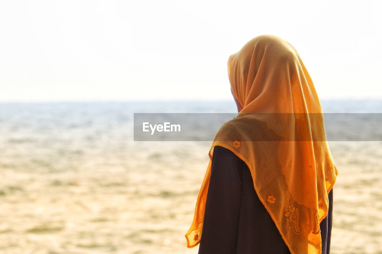 Side view of teenage girl wearing hijab standing at beach against clear sky