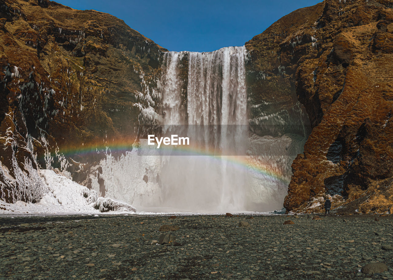 SCENIC VIEW OF WATERFALL AGAINST RAINBOW IN SKY
