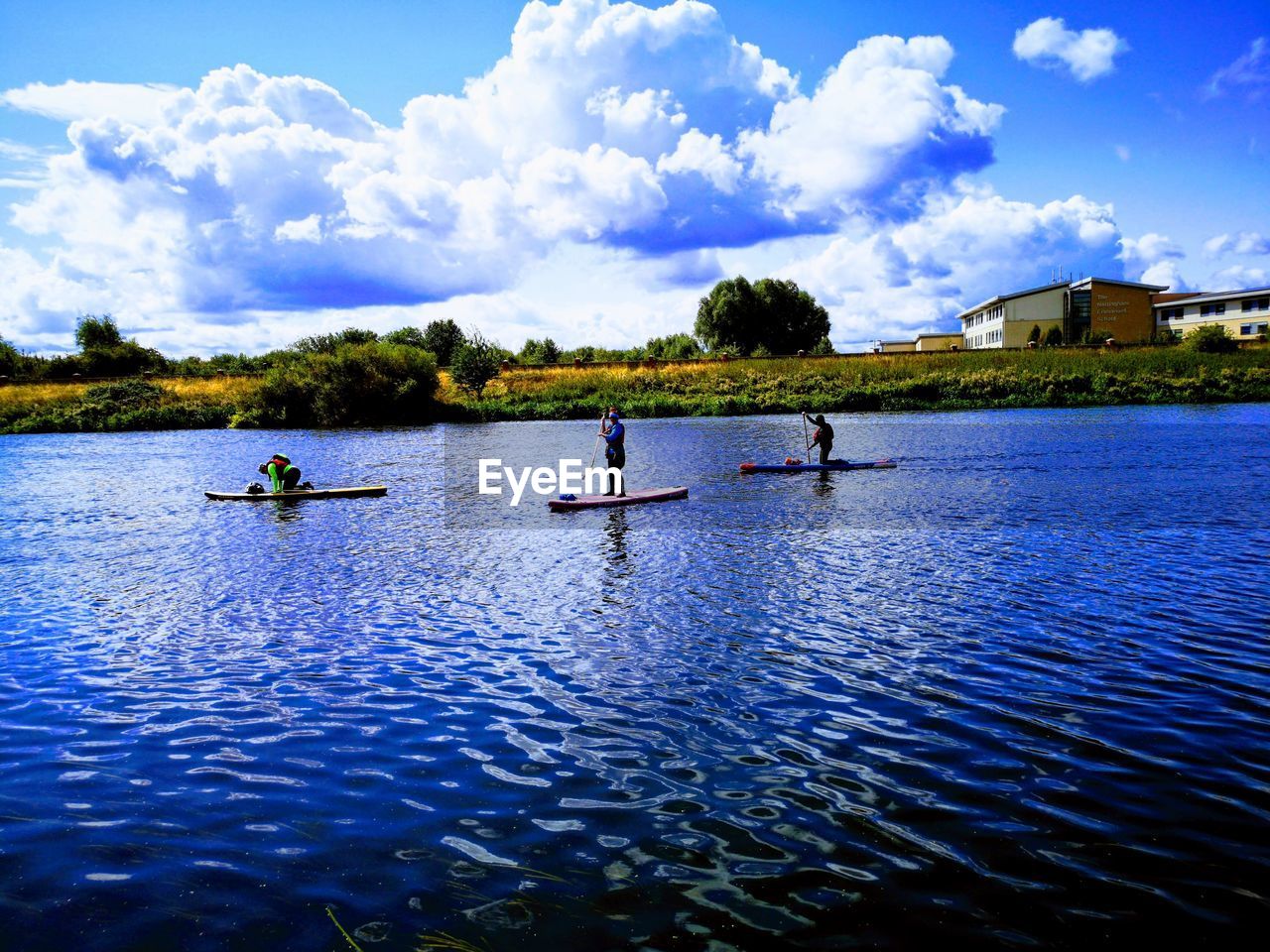 Male friends paddleboarding in river against cloudy sky