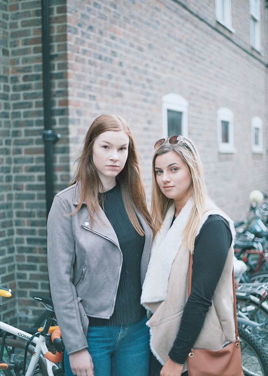 Portrait of young woman standing with friend outside building