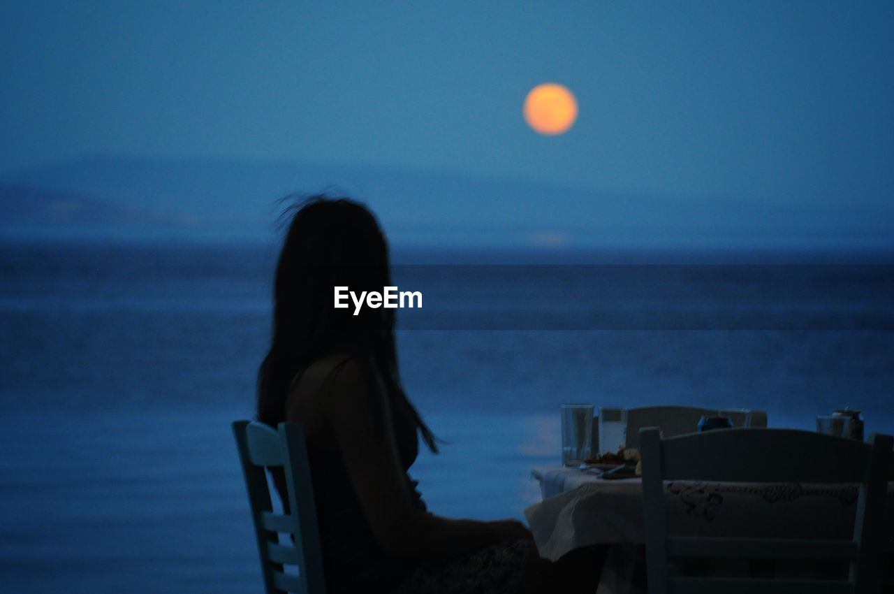 Side view of woman looking at sea against sky during dusk