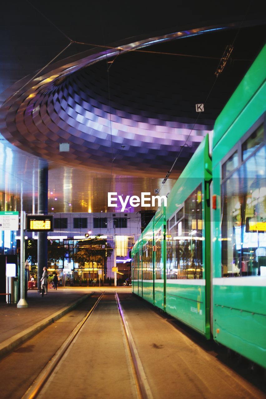 Green tramway on city street in illuminated city at night