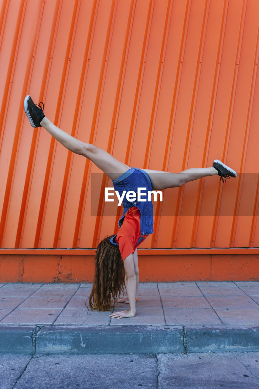 Young woman doing handstand against orange wall