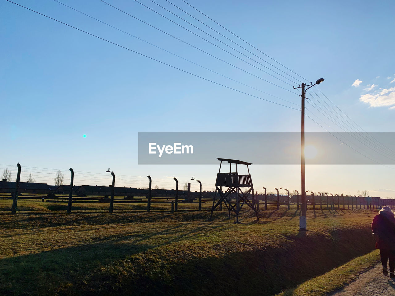 ELECTRICITY PYLON ON FIELD AGAINST SKY AT SUNSET