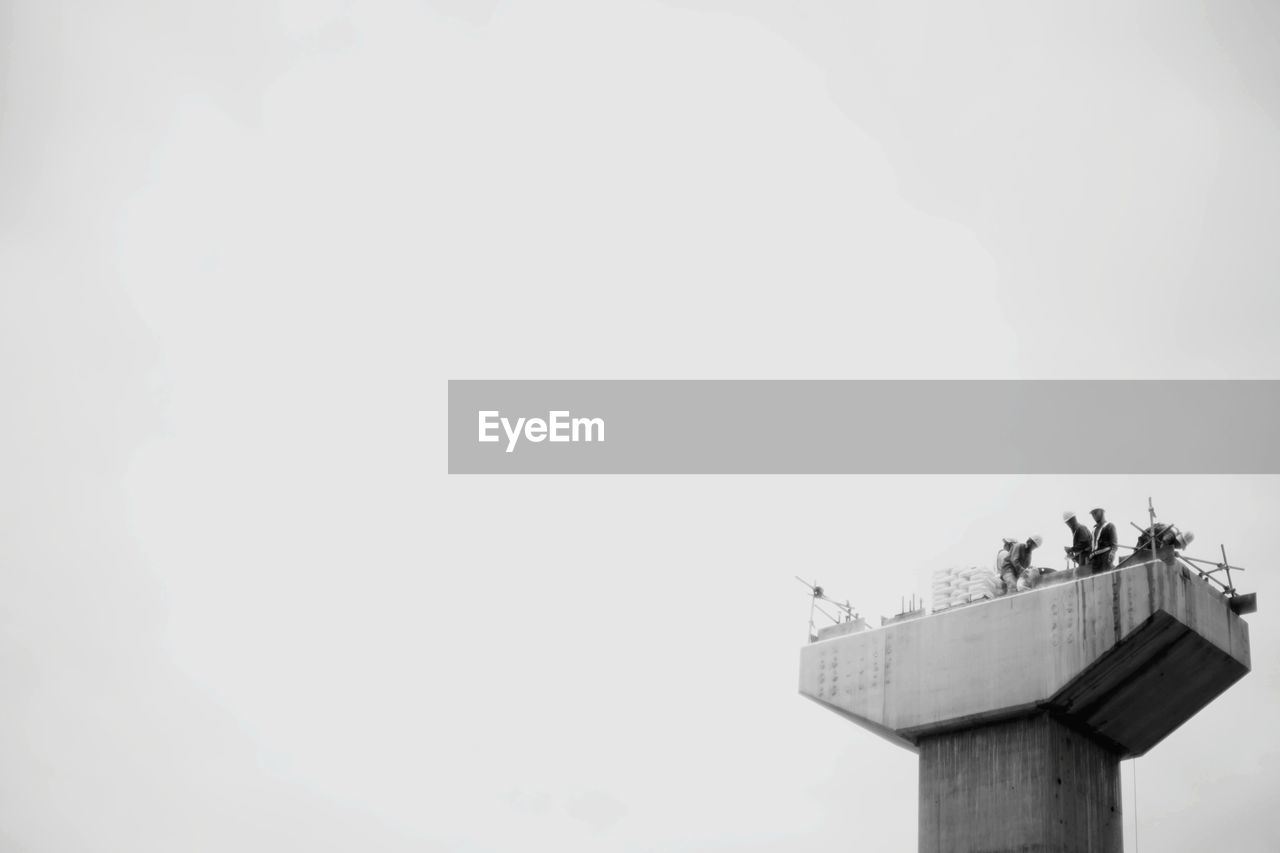 Low angle view of workers on built structure against clear sky