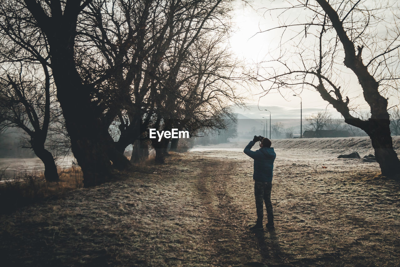 Man photographing bare trees in forest