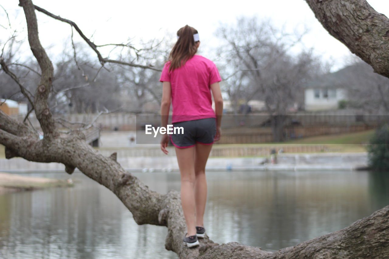 Rear view of woman walking on tree trunk by pond