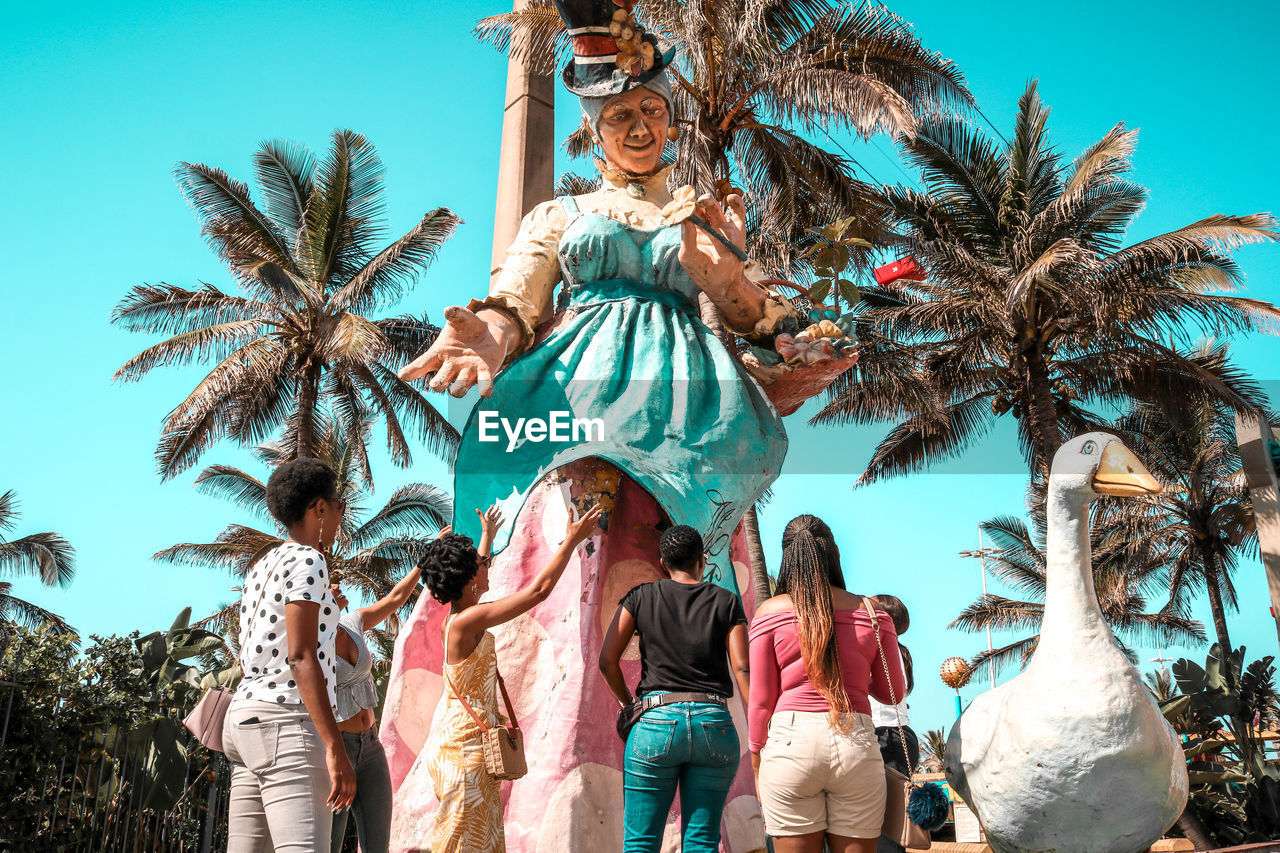 LOW ANGLE VIEW OF PEOPLE WITH PALM TREES