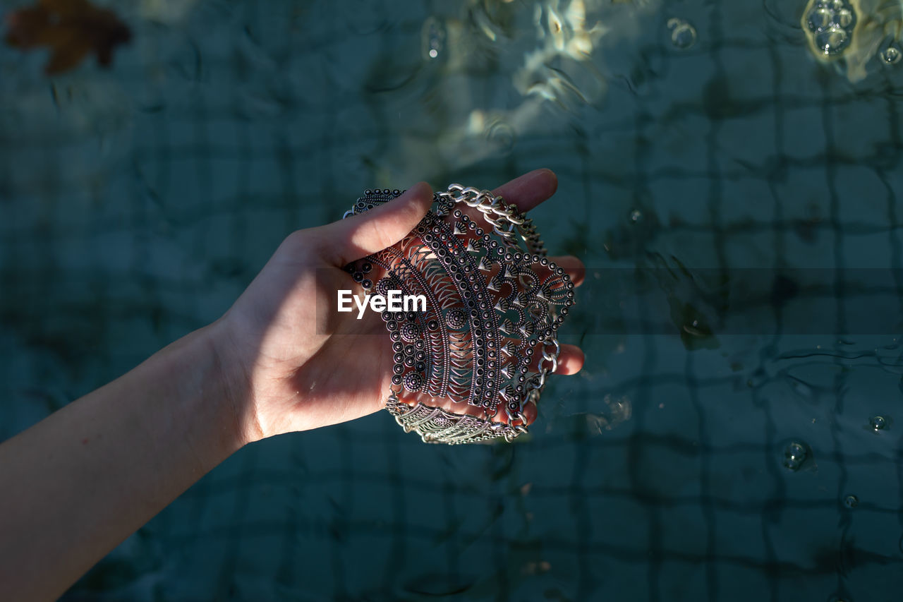 Close-up of hand holding jewelry over swimming pool