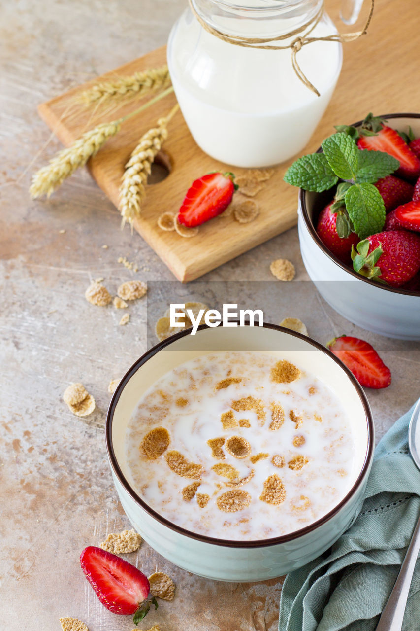 Healthy breakfast - whole grain flakes, milk and fresh strawberries on stone or slate background. 