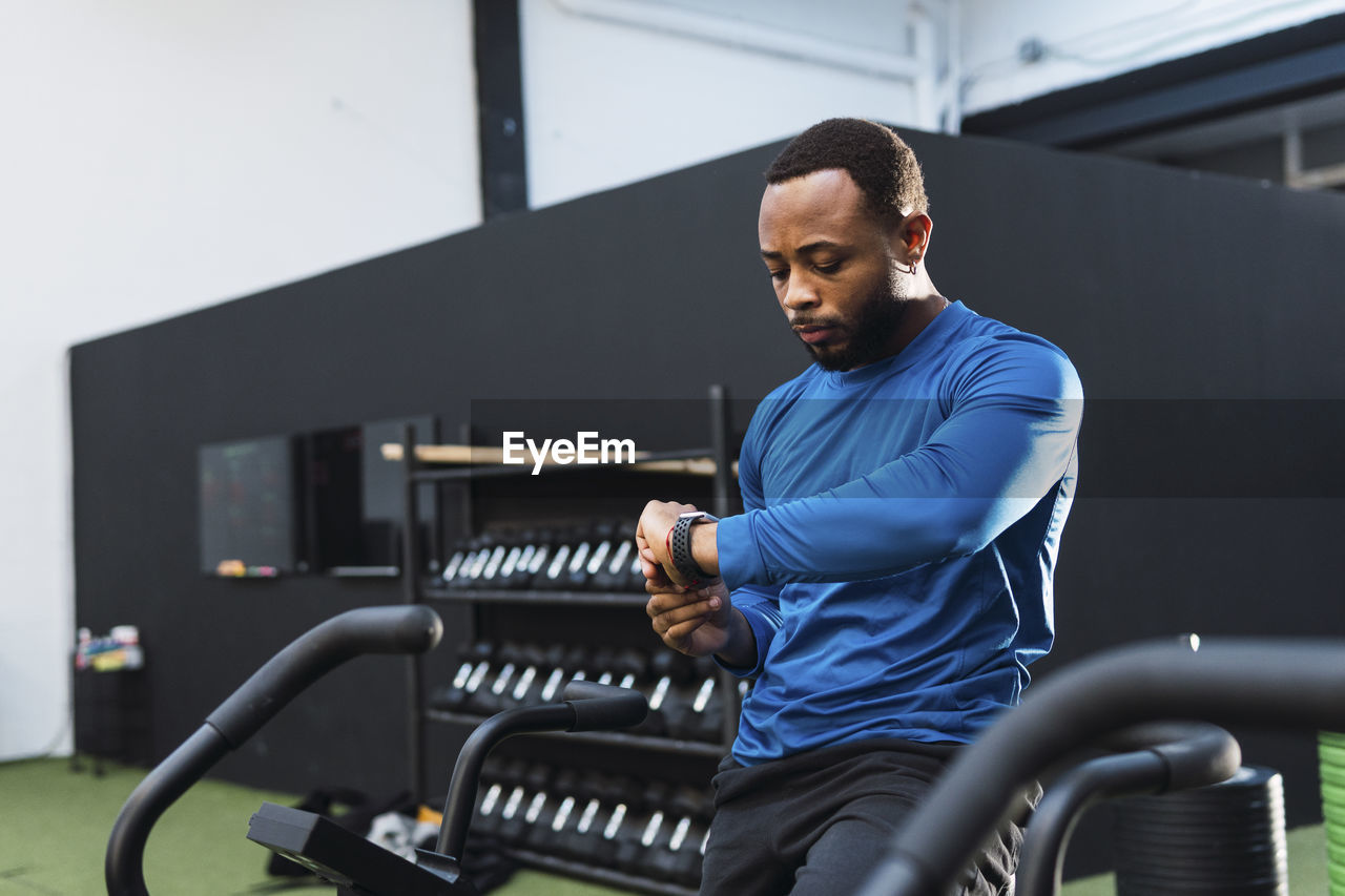 Athlete using fitness tracker sitting on airbike in gym