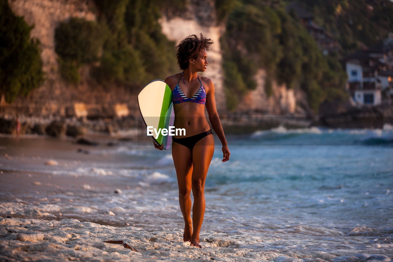 Full length of woman with surfboard walking at beach