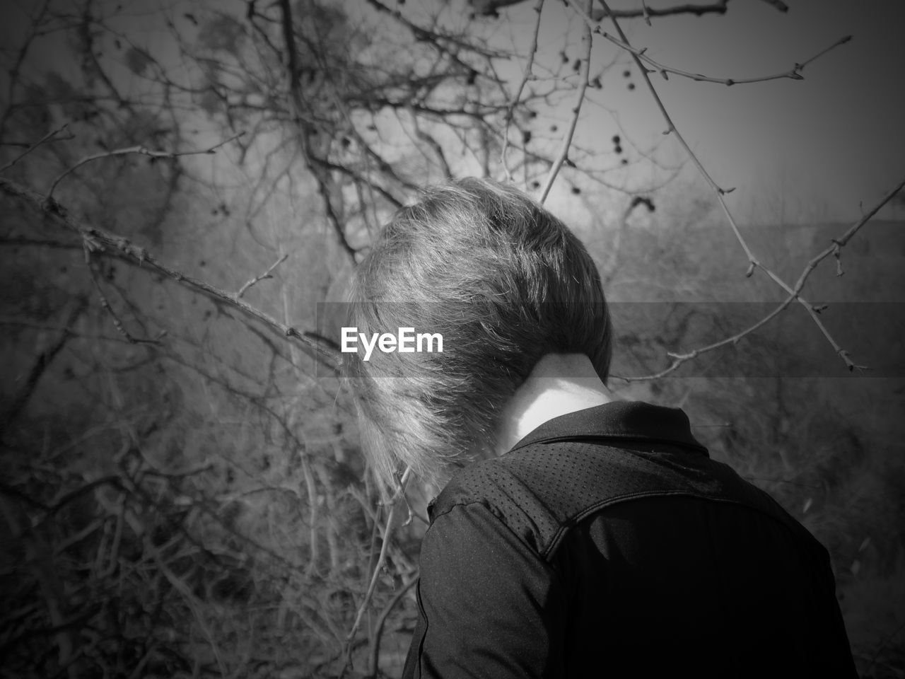 REAR VIEW OF MAN STANDING BY BARE TREES IN FOREST